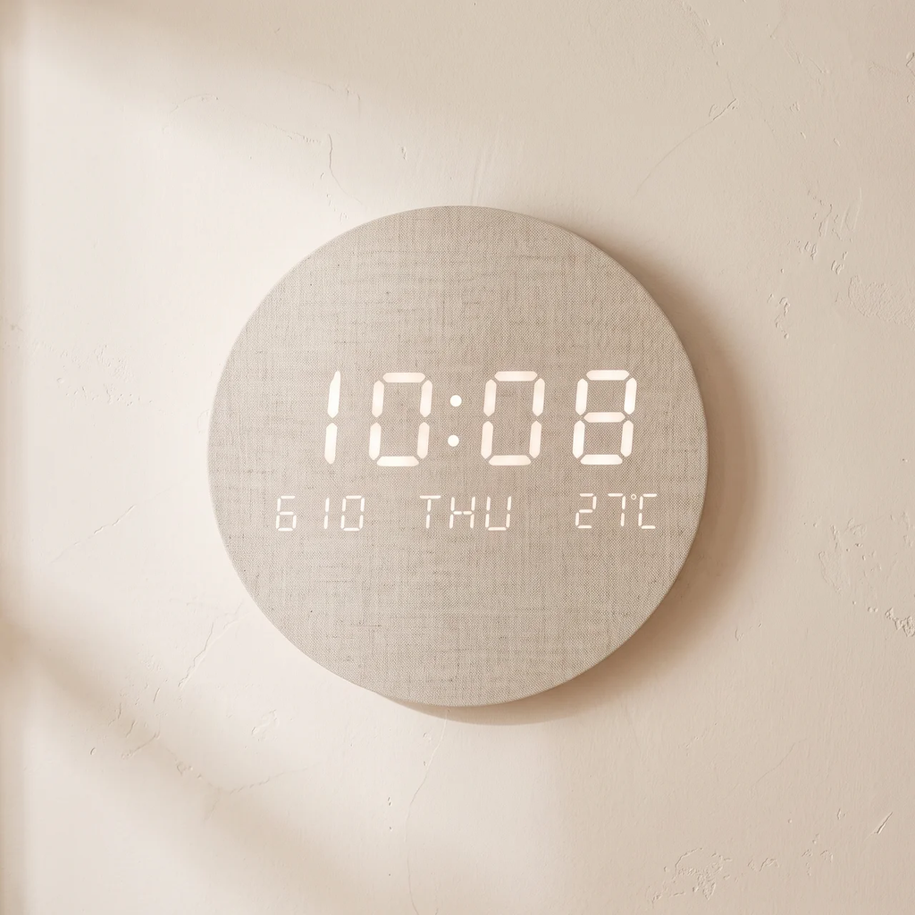A round digital wall clock with a light beige linen-textured face and white LED display, mounted on a warm beige wall.