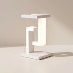 A modern white LED table lamp with a sculptural geometric design, featuring a glowing vertical light bar and a power bank base with a charging port, set against a minimalist beige background.