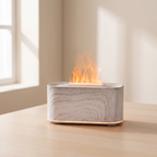 A rectangular tabletop electric fire pit with a light gray and white marble-look exterior and a glowing orange flame effect, sitting on a light wood table in a softly lit room.
