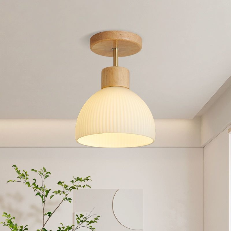 A modern ceiling light fixture with a ribbed white dome shade and natural wood accents, shown illuminated in a minimalist room setting.