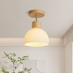 A modern ceiling light fixture with a ribbed white dome shade and natural wood accents, shown illuminated in a minimalist room setting.