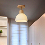 A modern semi-flush mount ceiling light with a ribbed white glass shade and light natural wood accents, shown illuminated in a minimalist hallway.