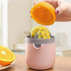 Pink manual juicer being used to extract juice from an orange on a wooden table.