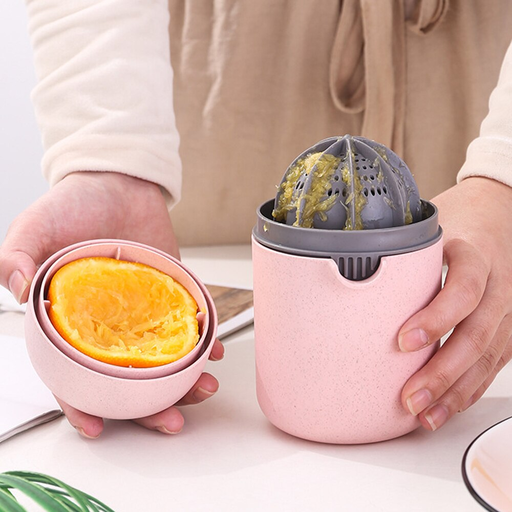 Pink manual juicer with a gray juicing basket holding an orange, being used by a person.