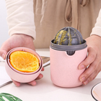 Pink manual juicer with a gray juicing basket holding an orange, being used by a person.