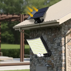 Solar-powered outdoor security light mounted on a stone pillar under a beige roof, with a small solar panel above and yellow arrows indicating sunlight. The light has a black frame and a large white LED panel.