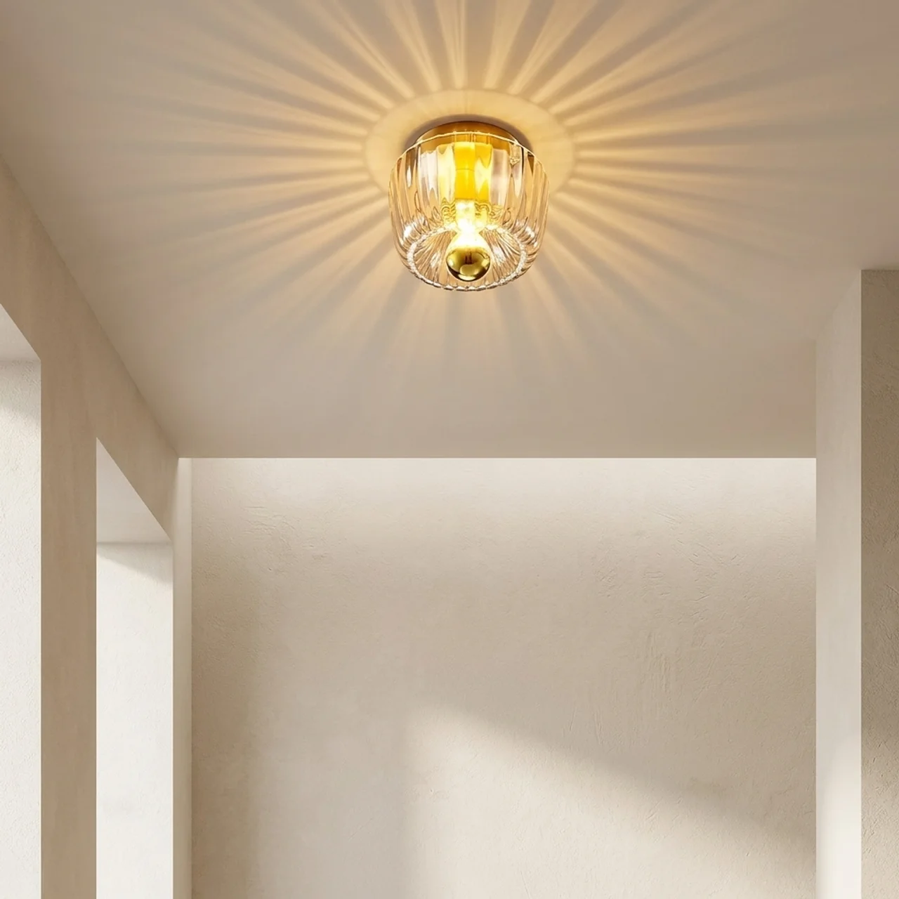A ceiling-mounted light fixture with a clear ribbed glass shade and warm yellow-gold metal trim, glowing with sunburst rays on a beige interior wall.