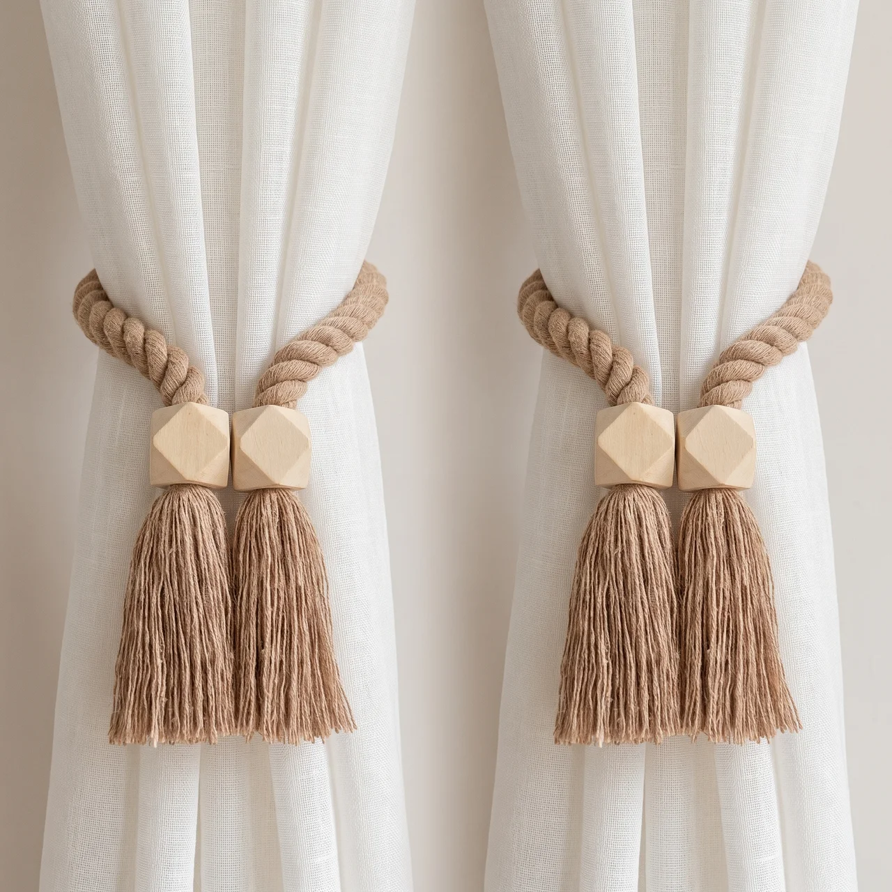 Two beige rope curtain tiebacks with geometric wooden connectors and long tassels, shown hanging on white sheer curtains.