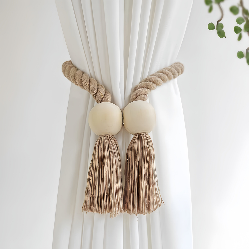 A bohemian-style curtain tieback featuring a thick braided jute rope, two round wooden beads, and matching tassels, shown tied around a white curtain.