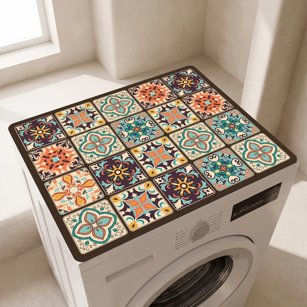 A rectangular floor mat with a colorful Mediterranean-style tile pattern sits on top of a white front-loading washing machine in a sunlit room.