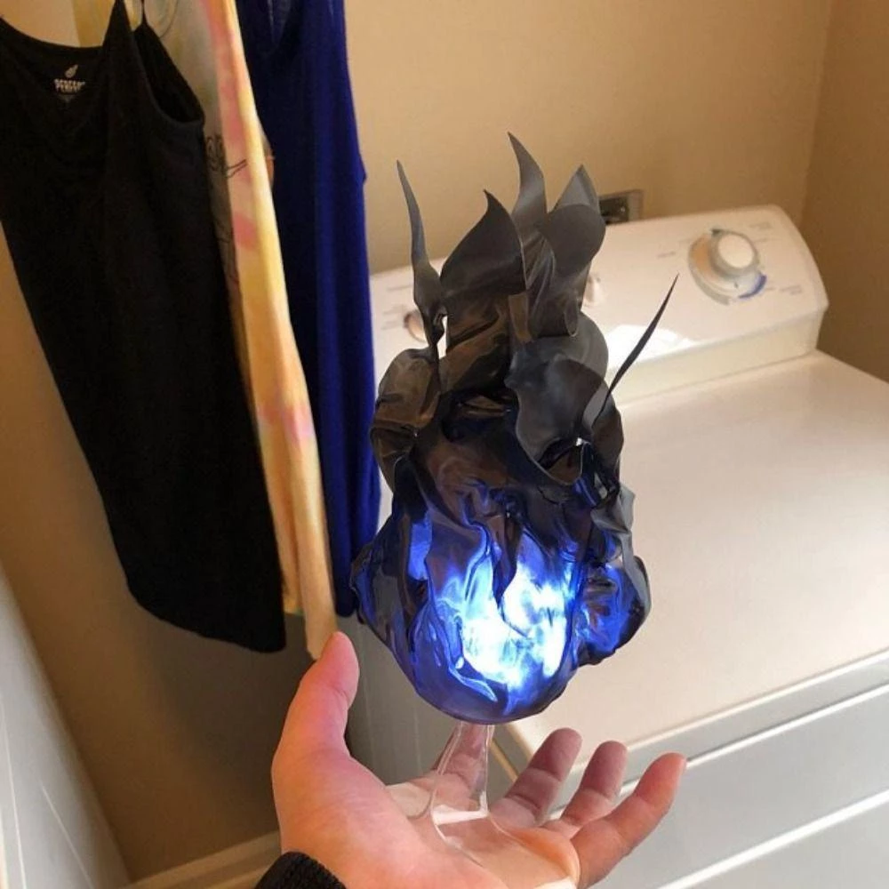 Hand holding a glowing blue and black dragon-shaped object in a laundry room.
