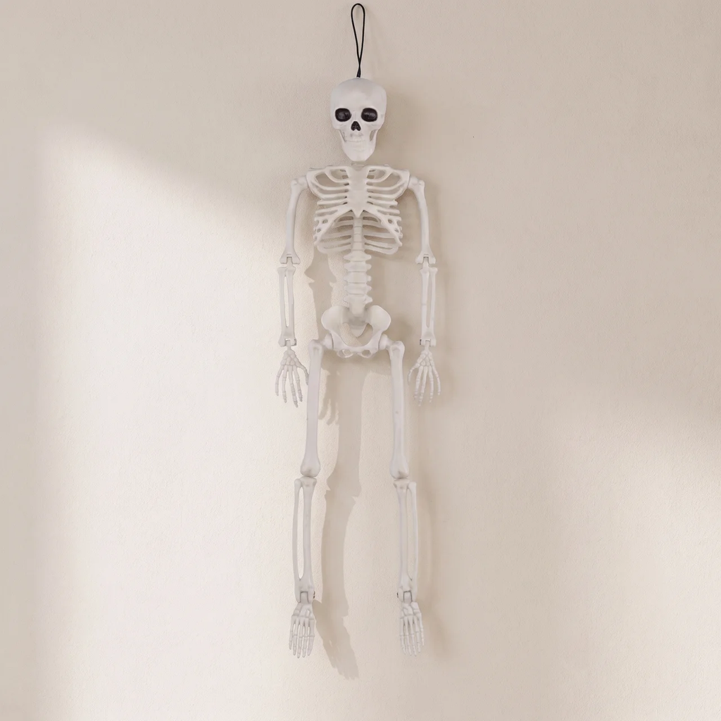 A hanging white plastic skeleton decoration with a black hanging loop at the top, shown against a plain off-white wall.