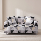 A modern two-seater sofa with a geometric triangle pattern in black, gray, white, and beige, styled in a minimalist room with beige walls and a light-colored rug.