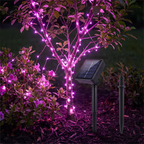 Solar-powered pink LED string lights wrapped around a small tree in a garden, with two black ground stakes shown beside the light unit.