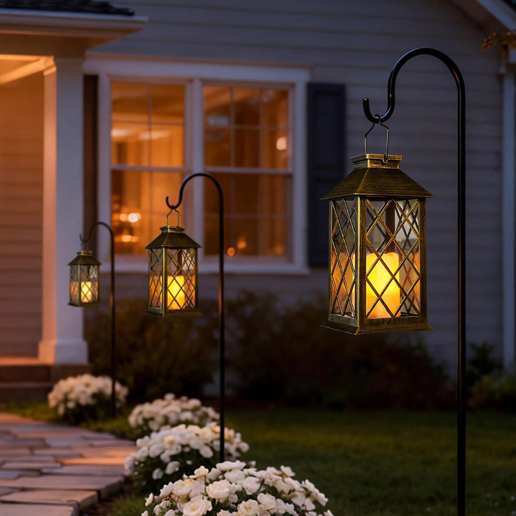 Decorative outdoor lanterns hanging from poles in front of a house at night.