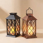 Two decorative lanterns with lit candles, one in matte black and one in distressed brown, standing on a beige surface against a matching beige background.