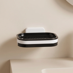 A black and white wall-mounted soap dish with a slotted tray, mounted on a beige wall above a sink.