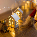 Decorative string lights with a small house-shaped lantern, teddy bear, and gnome on a wooden surface.
