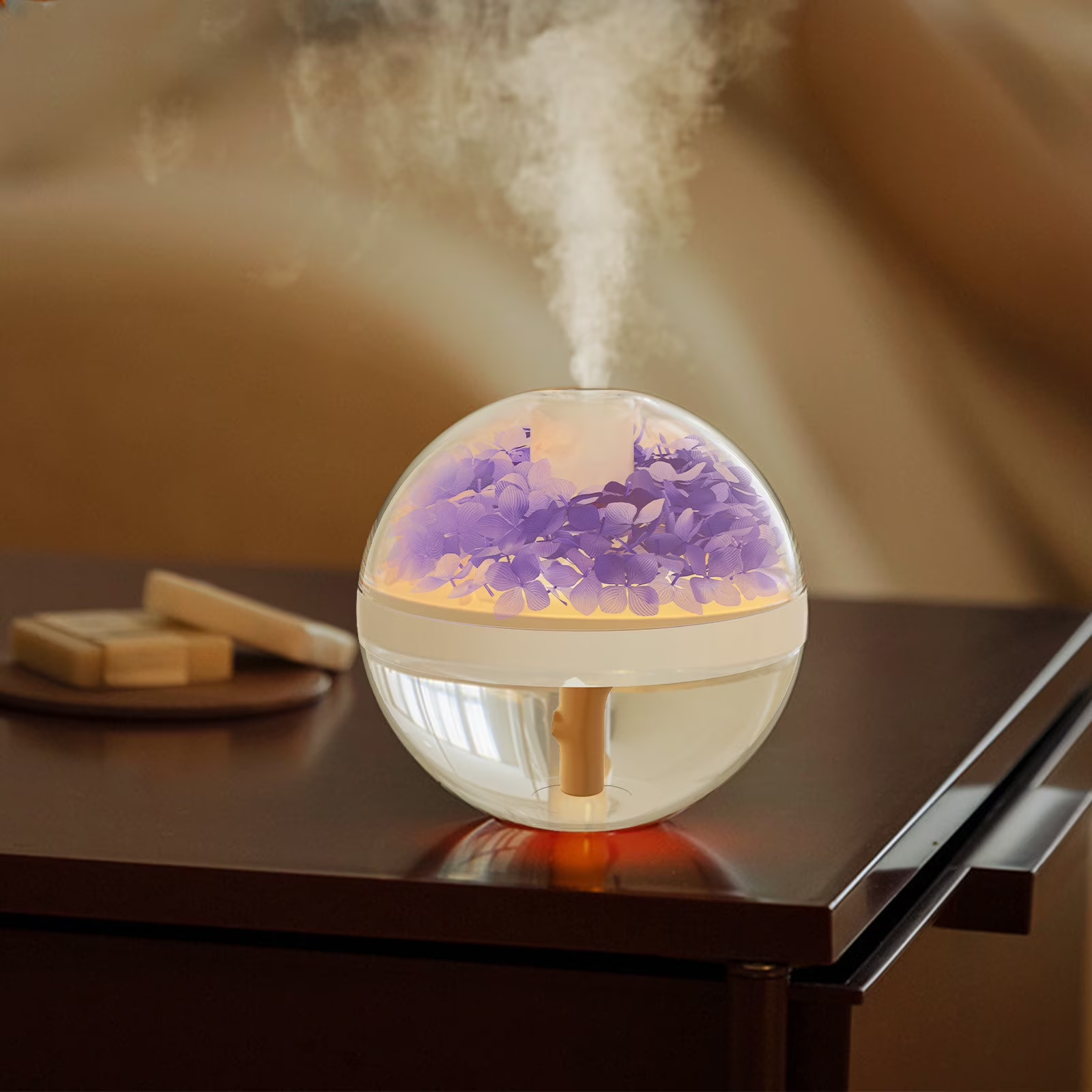 A spherical humidifier or diffuser sits on a dark wooden table, emitting a visible plume of steam. The device has a clear upper dome filled with purple dried flowers and a warm yellow light inside, with a clear lower half and a small wooden diffuser wand.