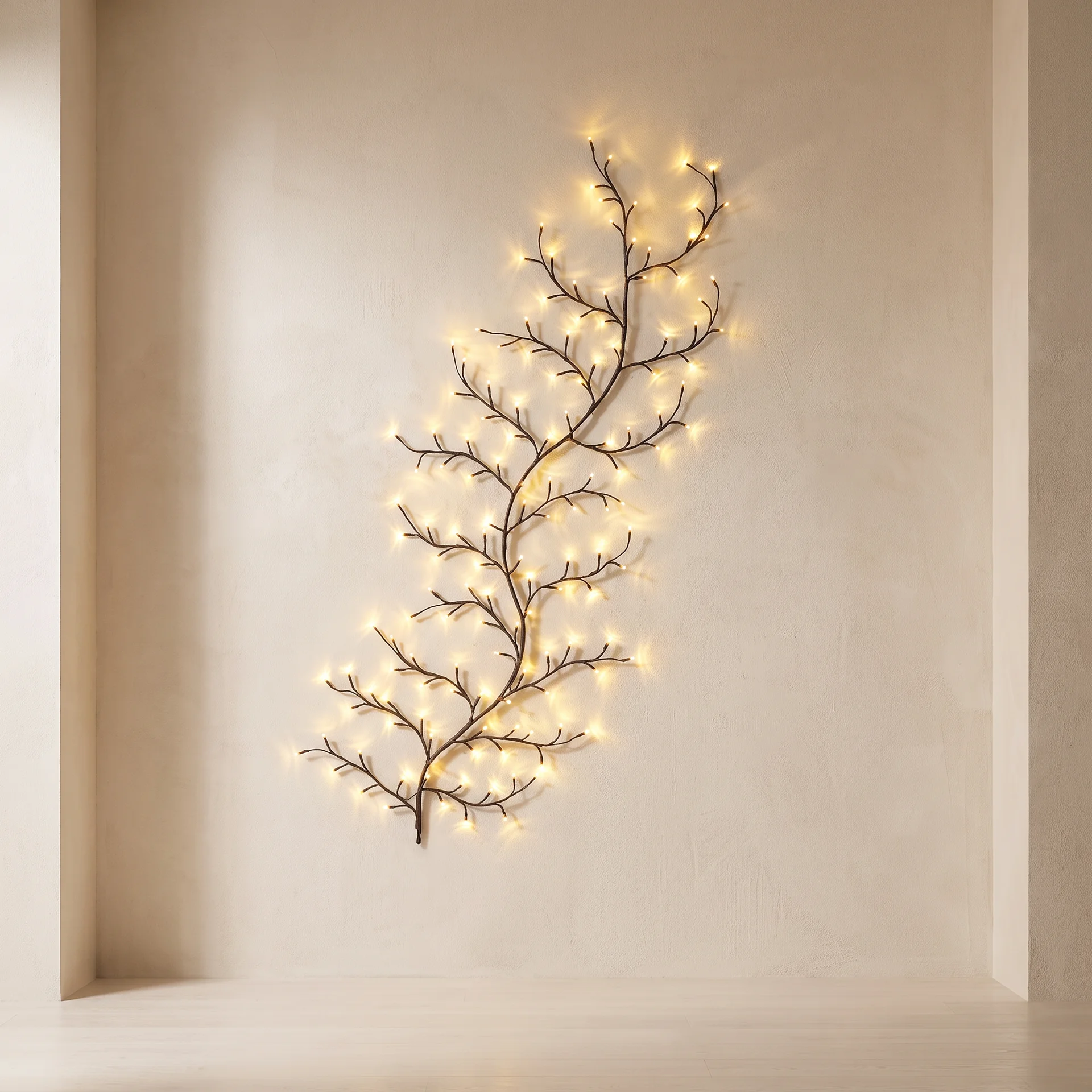 A decorative branch-shaped wall light with warm white fairy lights, mounted on a beige plaster wall in a minimalist interior setting.