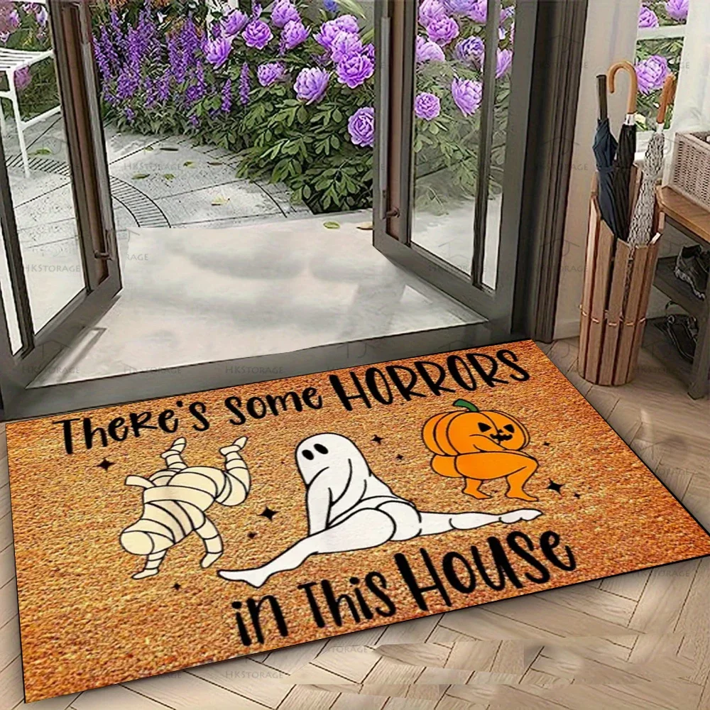 A rectangular Halloween doormat with a textured orange-brown background, featuring cartoon illustrations of a mummy, a ghost, and a pumpkin, with the text 'There's some HORRORS in this House' in black. The mat is shown placed at the threshold of a house, looking out onto a garden with purple flowers.
