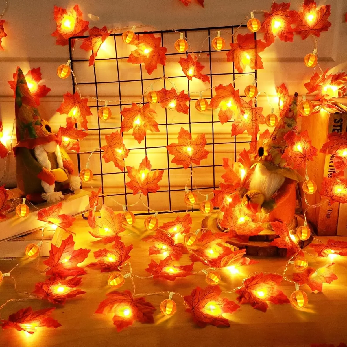 Warm white LED string lights with red and orange artificial maple leaves, decorated around a black wire grid and gnome figurines in a cozy indoor setting.