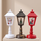 Three decorative table lanterns with holiday designs, shown side by side on a beige pedestal against a beige background. The lanterns are white, dark brown, and red, each with a Santa-themed window display.