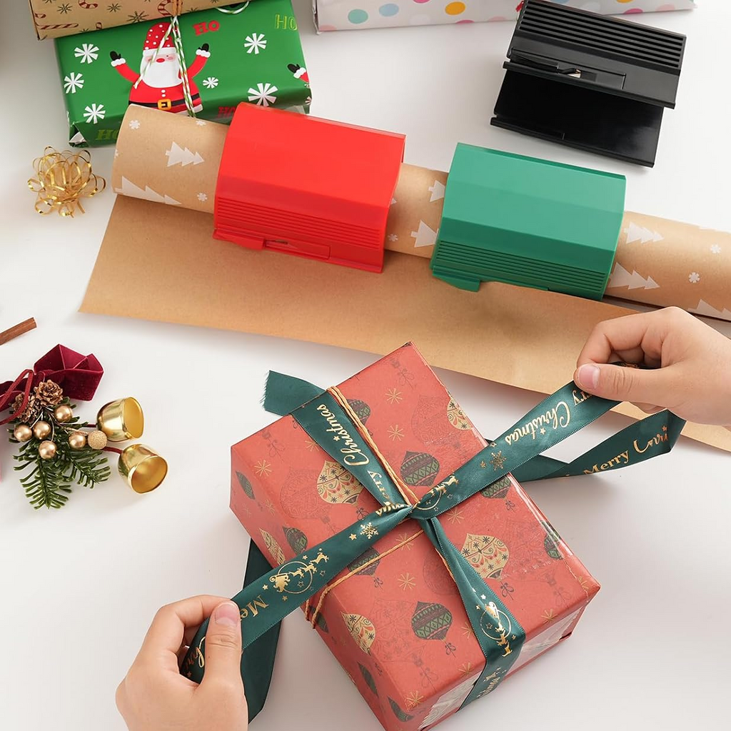 Person wrapping a gift with red paper and green ribbon on a white surface with Christmas decorations.