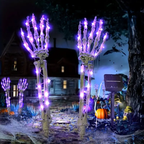 Halloween yard decorations featuring two large illuminated skeleton hands with glowing purple lights, set in a spooky garden scene at night with a house, tree, pumpkins, and cobwebs.