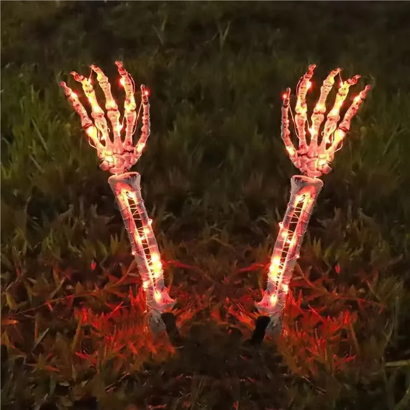 Two skeleton hand yard lights with glowing red and orange LED lights, planted in grass at night.