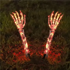Two skeleton hand yard lights with glowing red and orange LED lights, planted in grass at night.