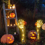 Halloween outdoor scene with glowing jack-o'-lantern pumpkins and illuminated skeleton hand yard lights arranged on the ground beside a rustic wooden ladder with candles.