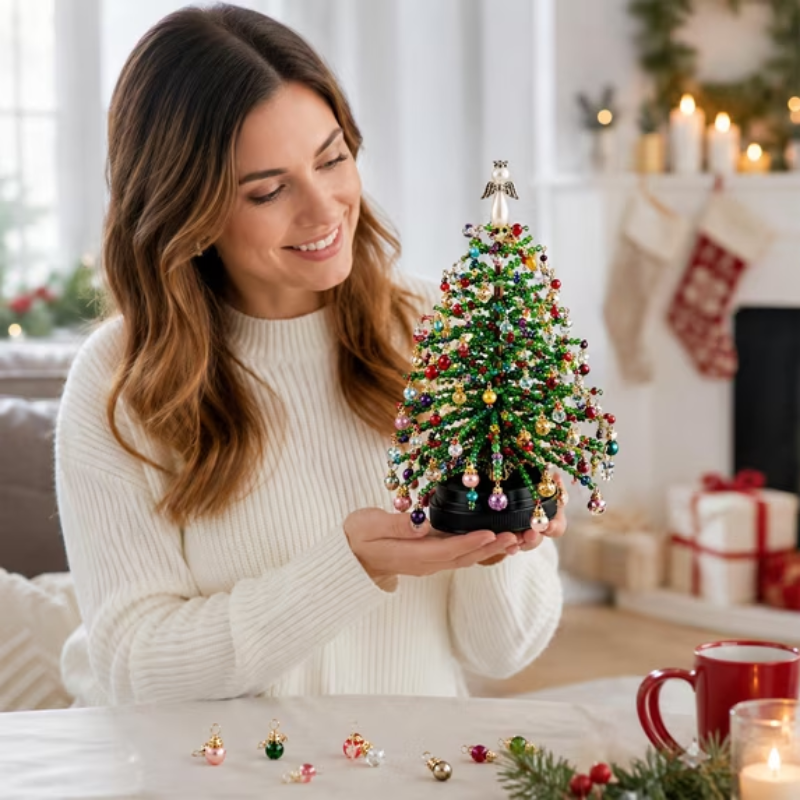 A woman in a white ribbed sweater holds a small decorated Christmas tree ornament in a cozy living room setting with stockings, gifts, and candles in the background.