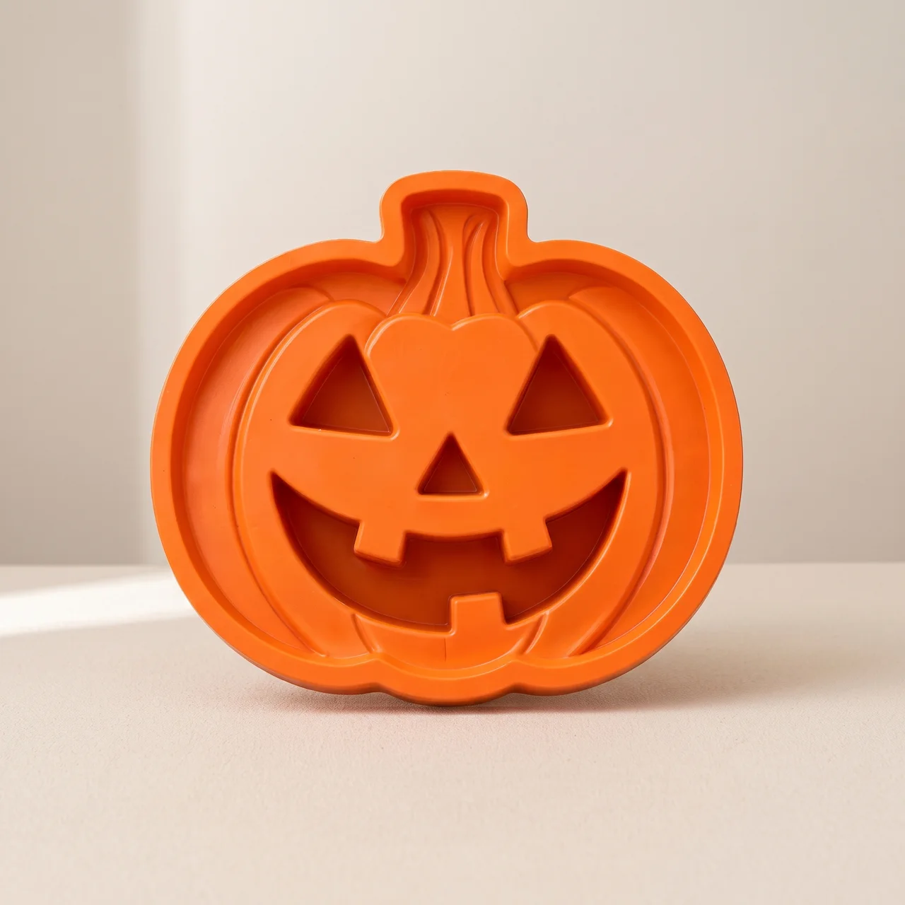 An orange pumpkin-shaped cookie cutter with a carved jack-o'-lantern face, shown on a neutral beige background.