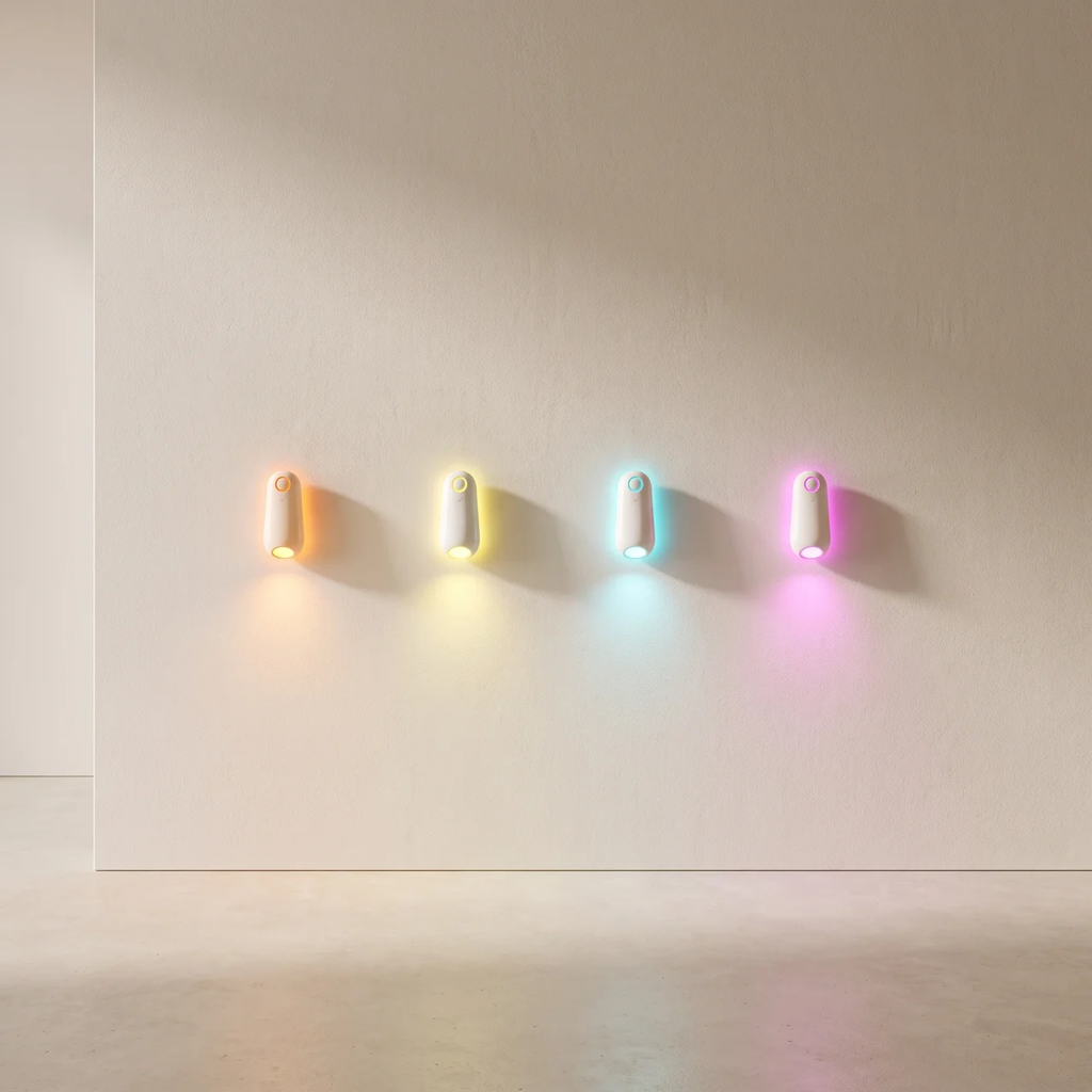 Four small cylindrical wall-mounted lights in different colors (orange, yellow, blue, pink) arranged in a row on a plain beige wall, casting soft light downwards.