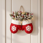 A festive Christmas wreath shaped like a pair of red mitten stockings hanging on a cream paneled door. The top of the wreath is decorated with artificial pine branches, white snowflakes, pinecones, red berries, and warm white string lights.