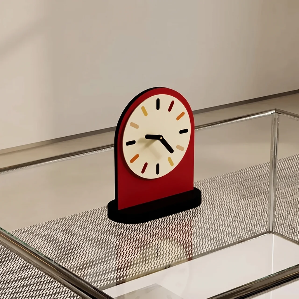A modern arch-shaped desk clock with a red body, cream dial face, and black hands, displayed on a glass tabletop with a mesh surface.