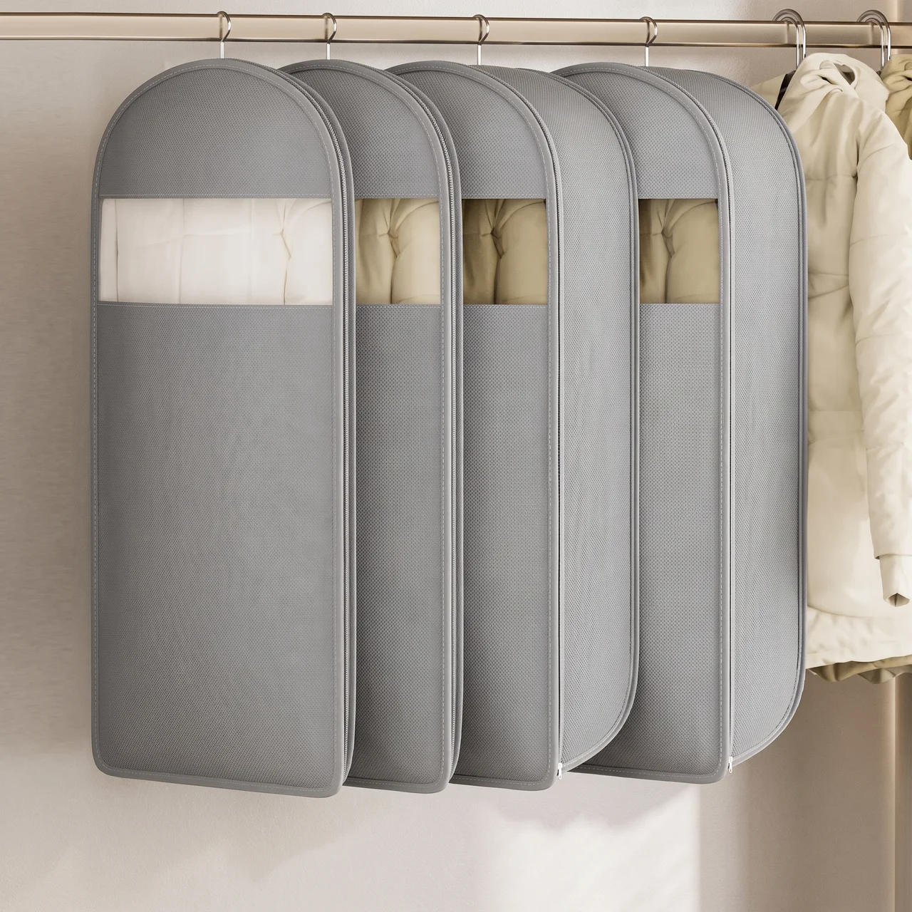 Four gray garment storage bags hanging on a closet rod, with a cream puffer jacket partially visible on the right side.