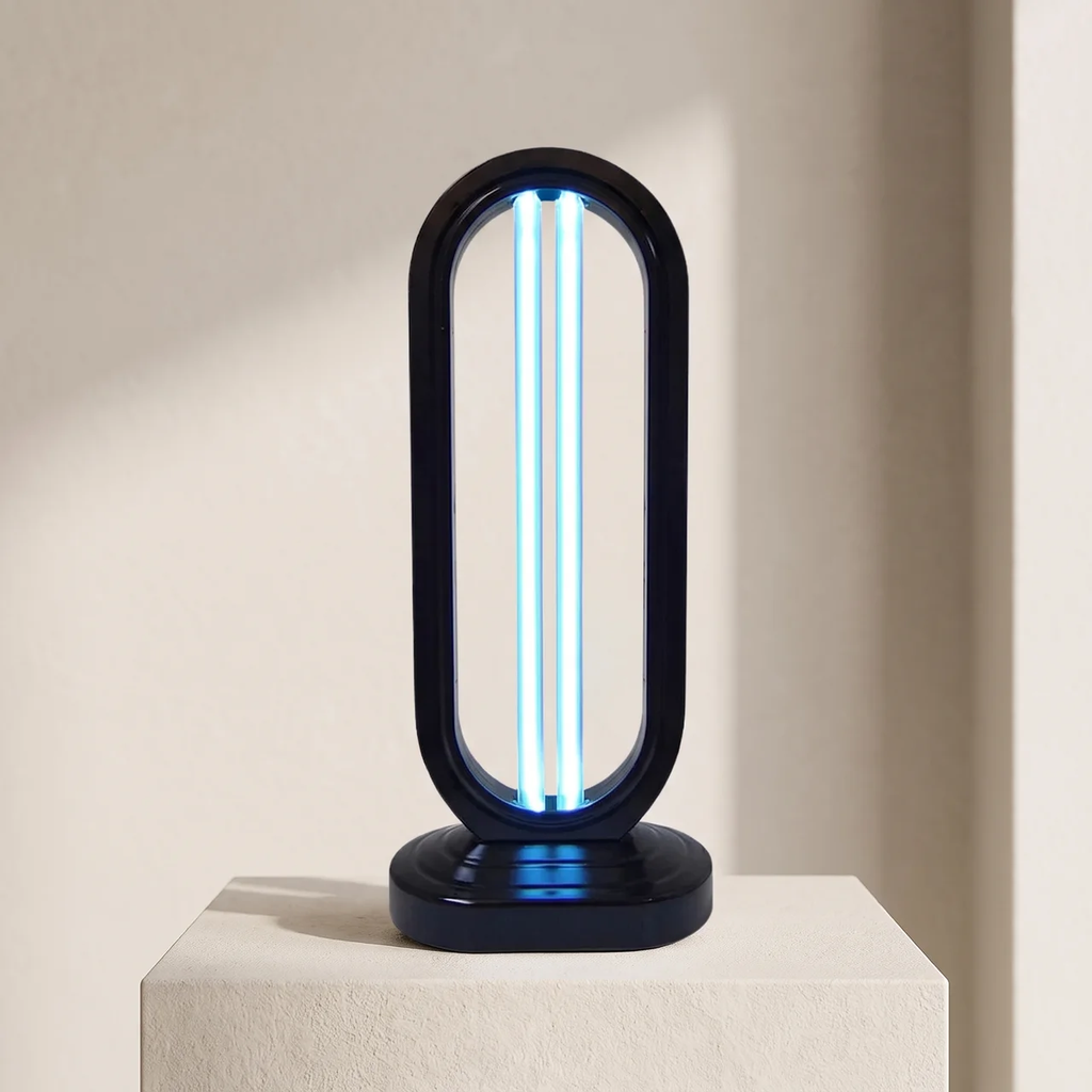 A modern black UV light table lamp with a glowing blue UV tube inside, displayed on a textured beige pedestal against a warm beige wall.