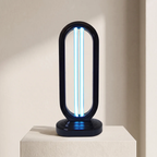 A modern black UV light table lamp with a glowing blue UV tube inside, displayed on a textured beige pedestal against a warm beige wall.
