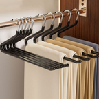 Black metal pants hangers with multiple hanging slots, shown hanging on a wooden closet rod with folded trousers in neutral colors.