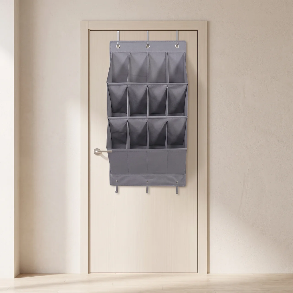 A gray fabric over-the-door hanging organizer with multiple compartments, shown hanging on a light beige door in a minimalist room setting.
