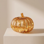 An amber glass pumpkin with embedded gold leaf flakes sits on a white display pedestal against a warm beige background.