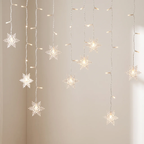 Warm white LED curtain string lights featuring hanging snowflake-shaped bulbs, shown illuminated against a plain beige wall.