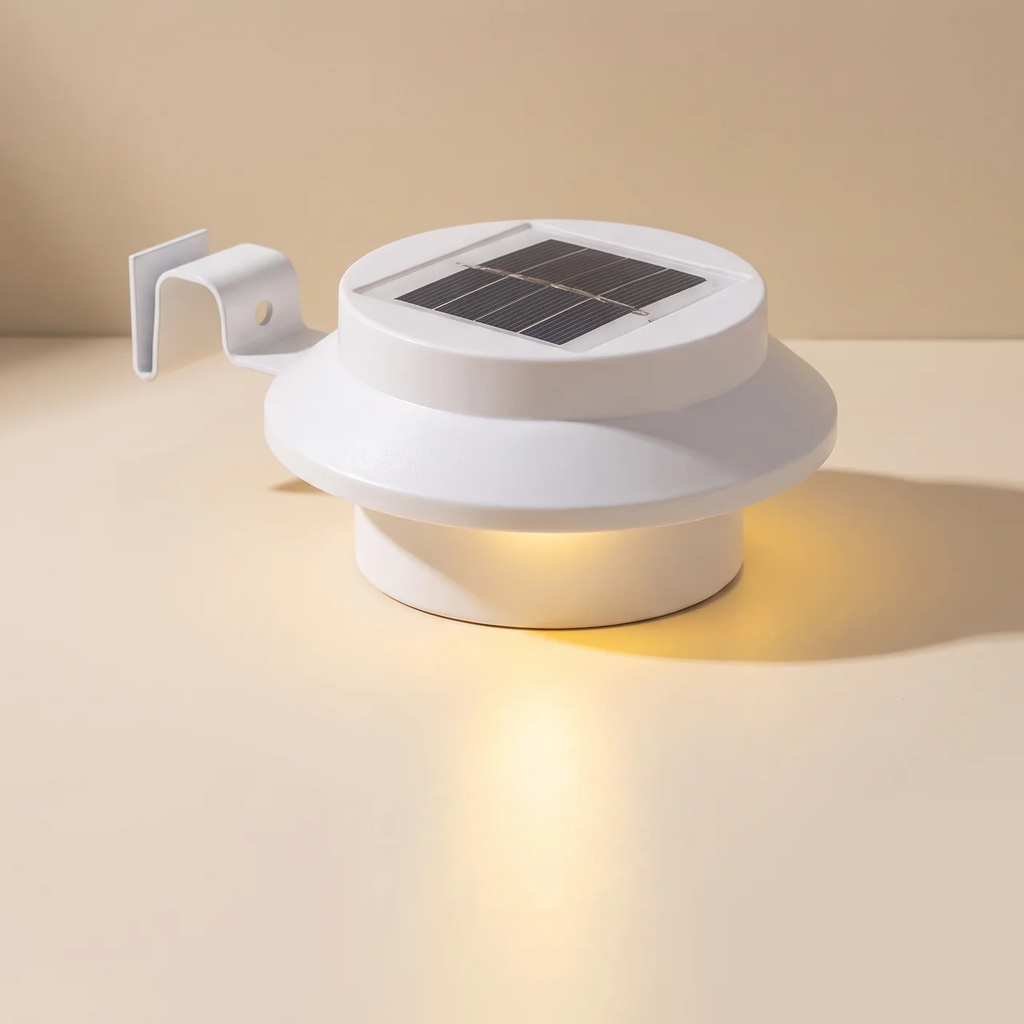 A white solar-powered outdoor light fixture with a circular top panel containing a dark solar cell and a side mounting bracket, shown lit on a warm beige background.