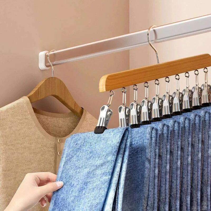 A close-up of a clothing hanger organizer in use, holding multiple blue garments on a wooden hanger suspended from a white closet rod. A hand is visible holding one of the blue fabric pieces.