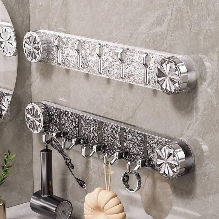 Two silver chrome wall-mounted toothbrush holder racks with decorative floral end caps and multiple hooks, shown mounted on a gray marble-look bathroom wall with toiletries hanging below.