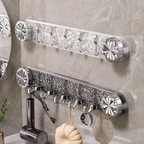 Two silver chrome wall-mounted toothbrush holder racks with decorative floral end caps and multiple hooks, shown mounted on a gray marble-look bathroom wall with toiletries hanging below.