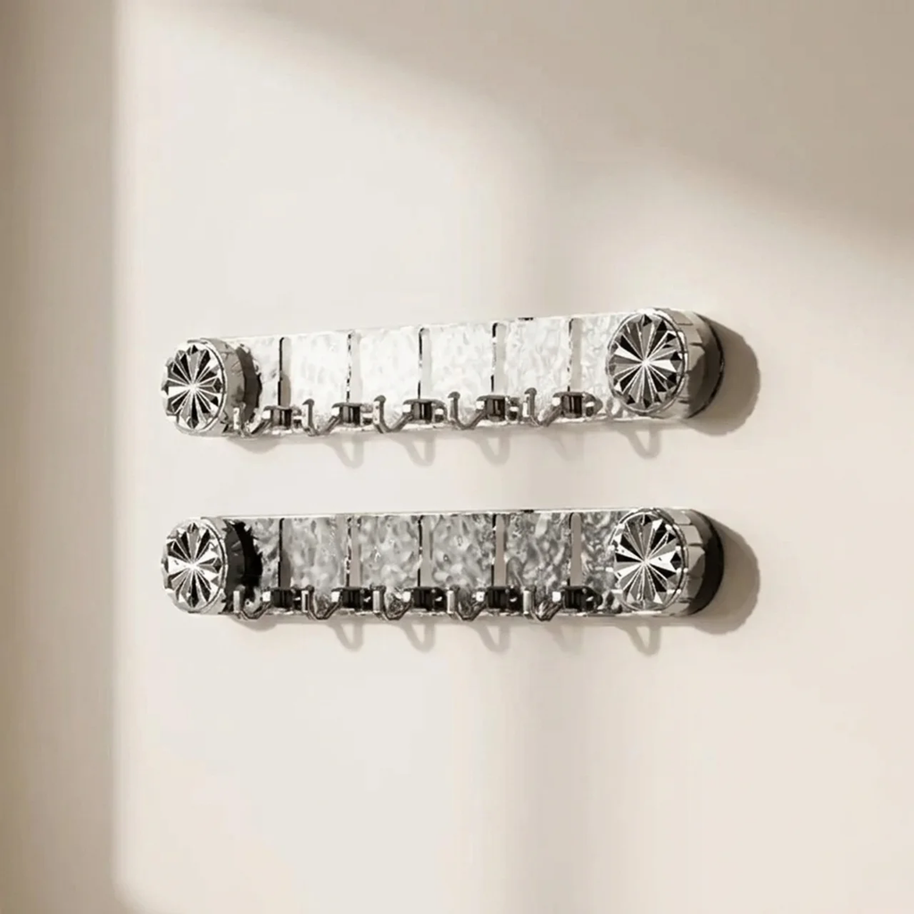 Two silver wall-mounted hook racks with decorative starburst end caps, shown hanging on a plain off-white wall.