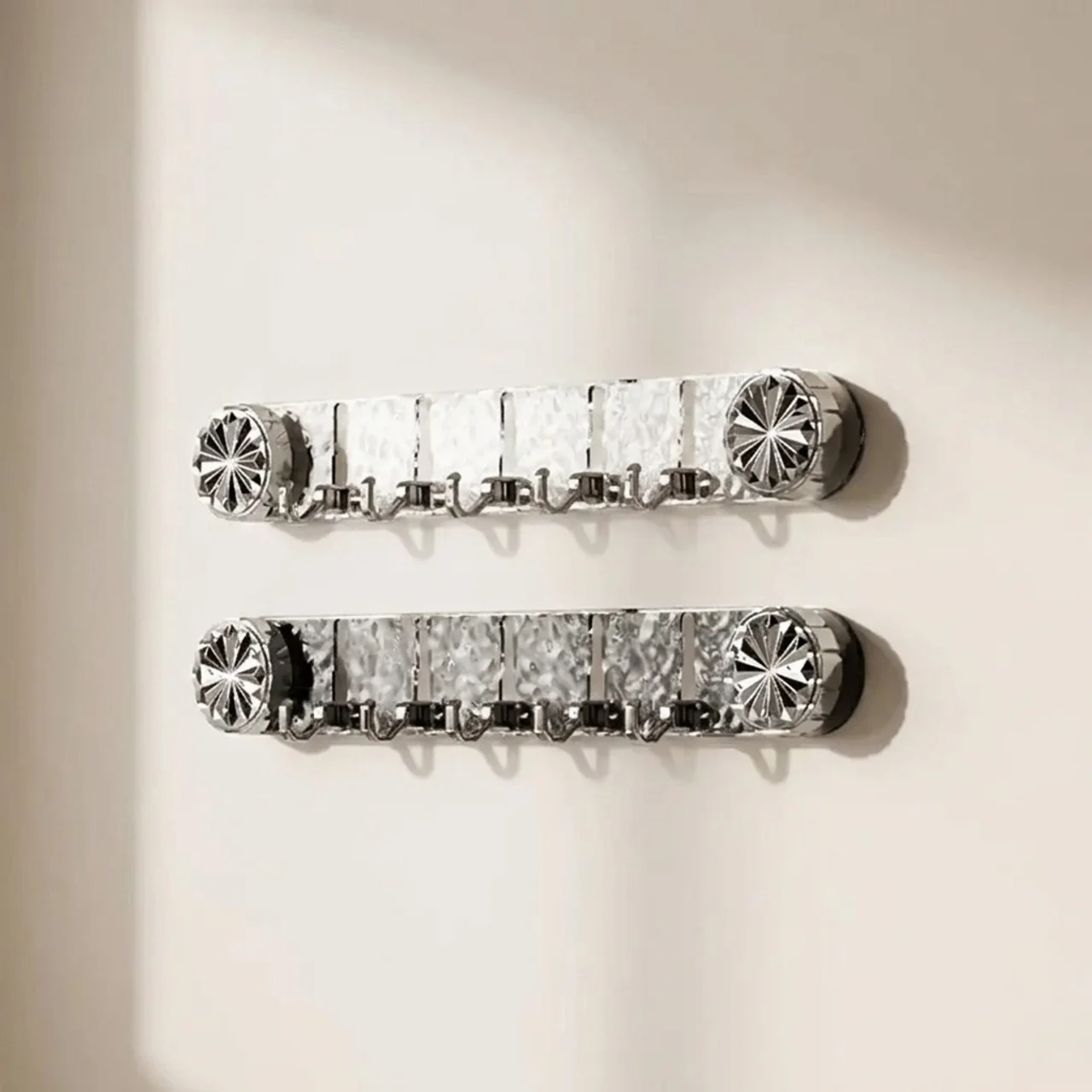 Two silver wall-mounted hook racks with decorative starburst end caps, shown hanging on a plain off-white wall.